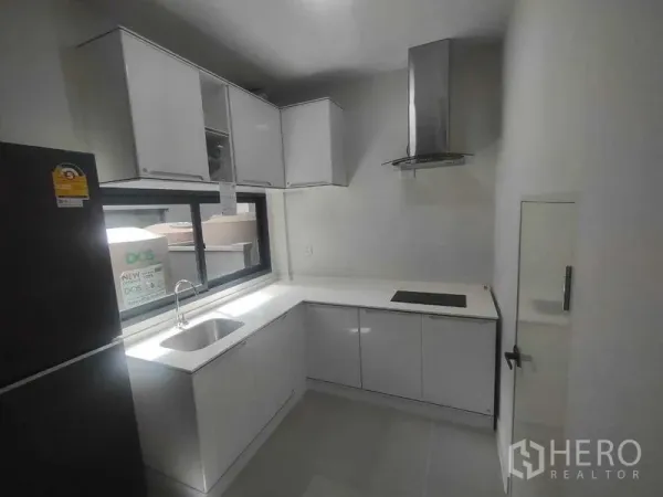 Detached House for rent in Khan Na Yao, Bangkok - Compact white L‑shaped kitchen with sink, window, cooktop and stainless range hood.