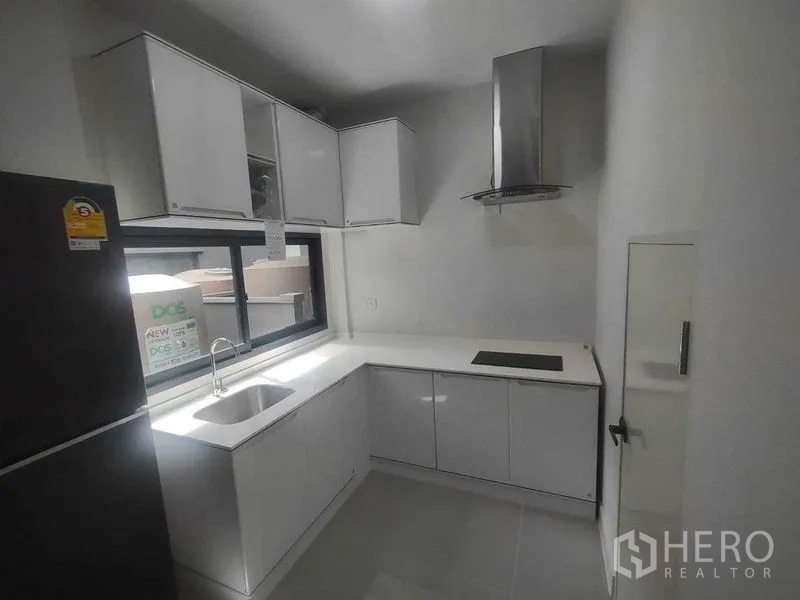 Detached House for rent in Khan Na Yao, Bangkok - Compact white L‑shaped kitchen with sink, window, cooktop and stainless range hood.