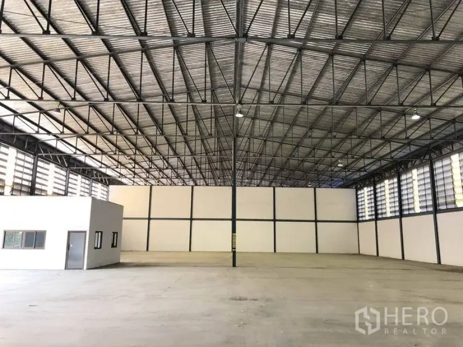 Warehouse for rent in Khlong Luang, Pathum Thani - Spacious warehouse interior with steel truss roof, concrete floor and a small office pod.