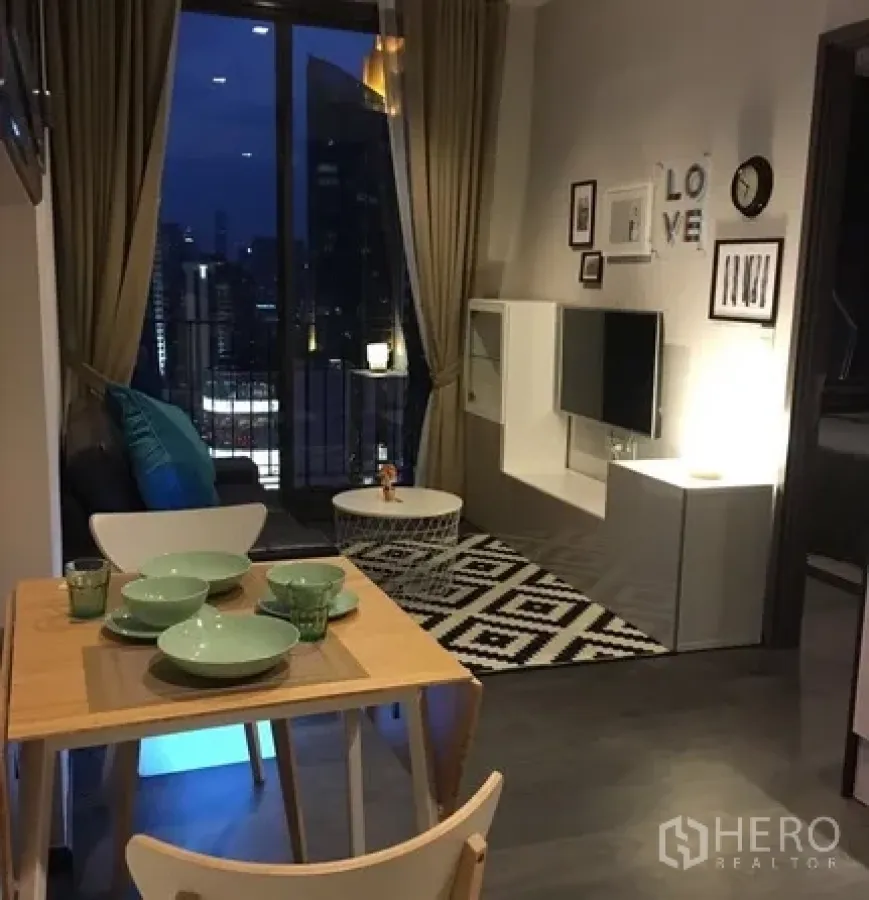 Condominium for rent in Watthana, Bangkok - Open-plan living and dining area with a balcony overlooking the Bangkok skyline at night.