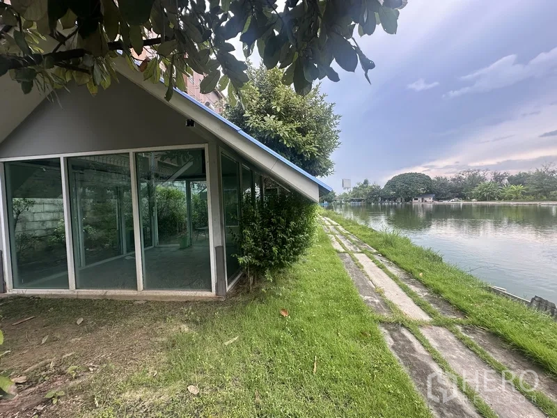 Standalone for rent in Prawet, Bangkok - Glass pavilion by the water with green lawn and lakeside path.