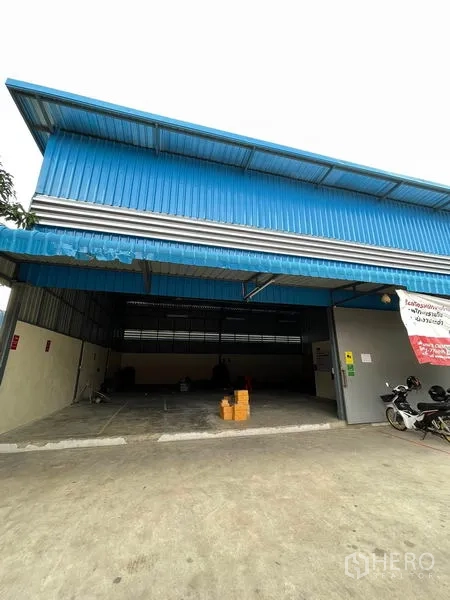 Warehouse for rent in Khlong Luang, Pathum Thani - Front facade with large sliding gate and parking apron for vans.