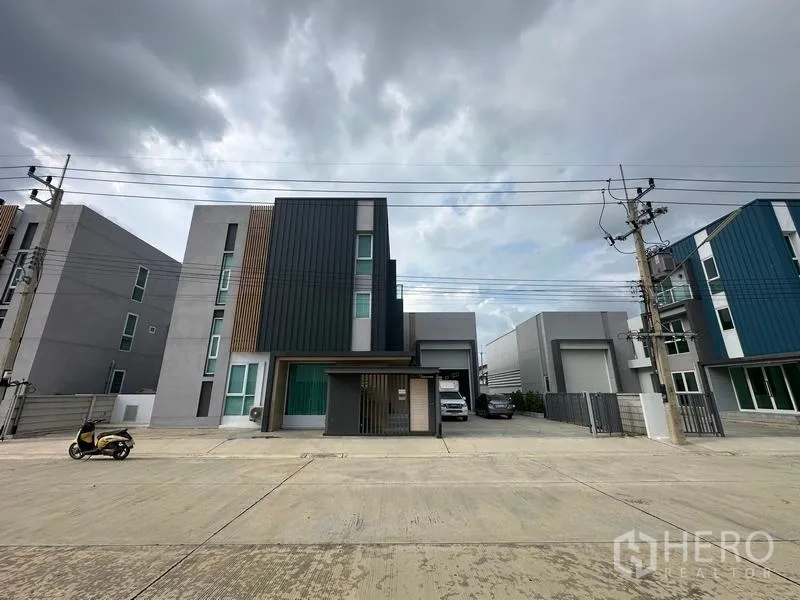 Warehouse for sale in Pathum Thani - Modern three-storey office facade with attached warehouse and gated parking on a wide road in Lam Luk Ka, Pathum Thani.
