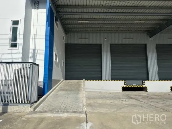 Factory for rent in Bang Sao Thong, Samut Prakan - Ramp to loading dock with covered bay and closed roller doors for truck access.