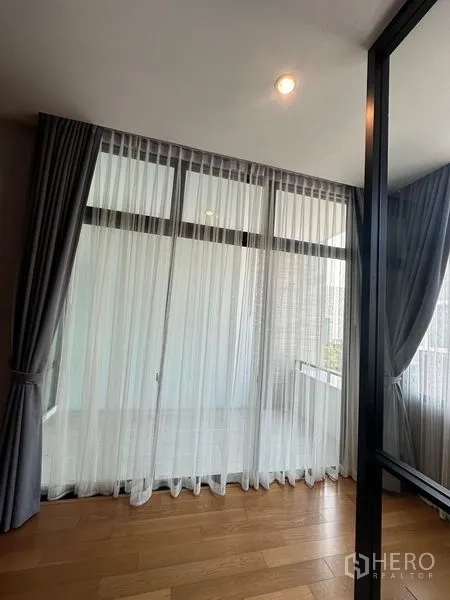 Townhouse for sale in Saphan Sung, Bangkok - Floor‑to‑ceiling windows with sheer curtains leading toward a small balcony.