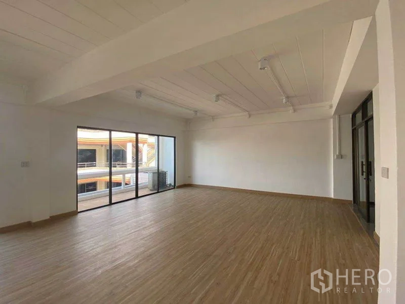 Office Space for rent in Watthana, Bangkok - Spacious 80 sqm office corner showing large windows, balcony access, and a white ceiling with track lights.