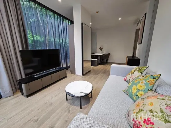 Condominium for rent or sale - Bright living room with sofa, TV console, and marble coffee table beside full-height curtains.