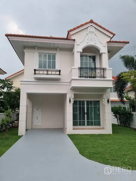 Detached House for sale in Nonthaburi - Two-storey detached house with red-tile roof, carport and a green front lawn.