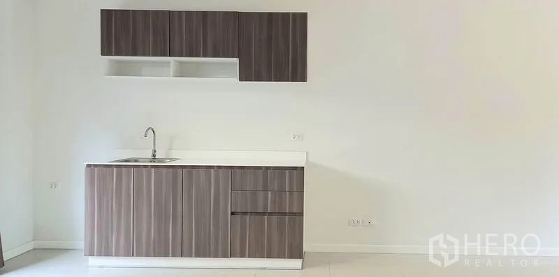Townhouse for sale in Mueang Pathum Thani, Pathum Thani - Compact pantry kitchen with wood-grain cabinets, white countertop, and single-bowl sink.