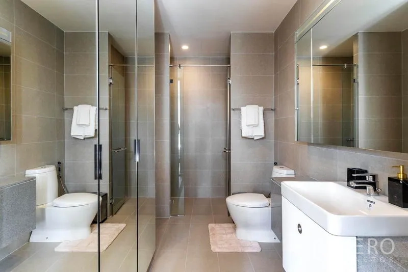 Condominium for rent in Pathum Wan, Bangkok - Contemporary bathroom in grey tiles with large mirror, glass shower enclosure and sleek fixtures.