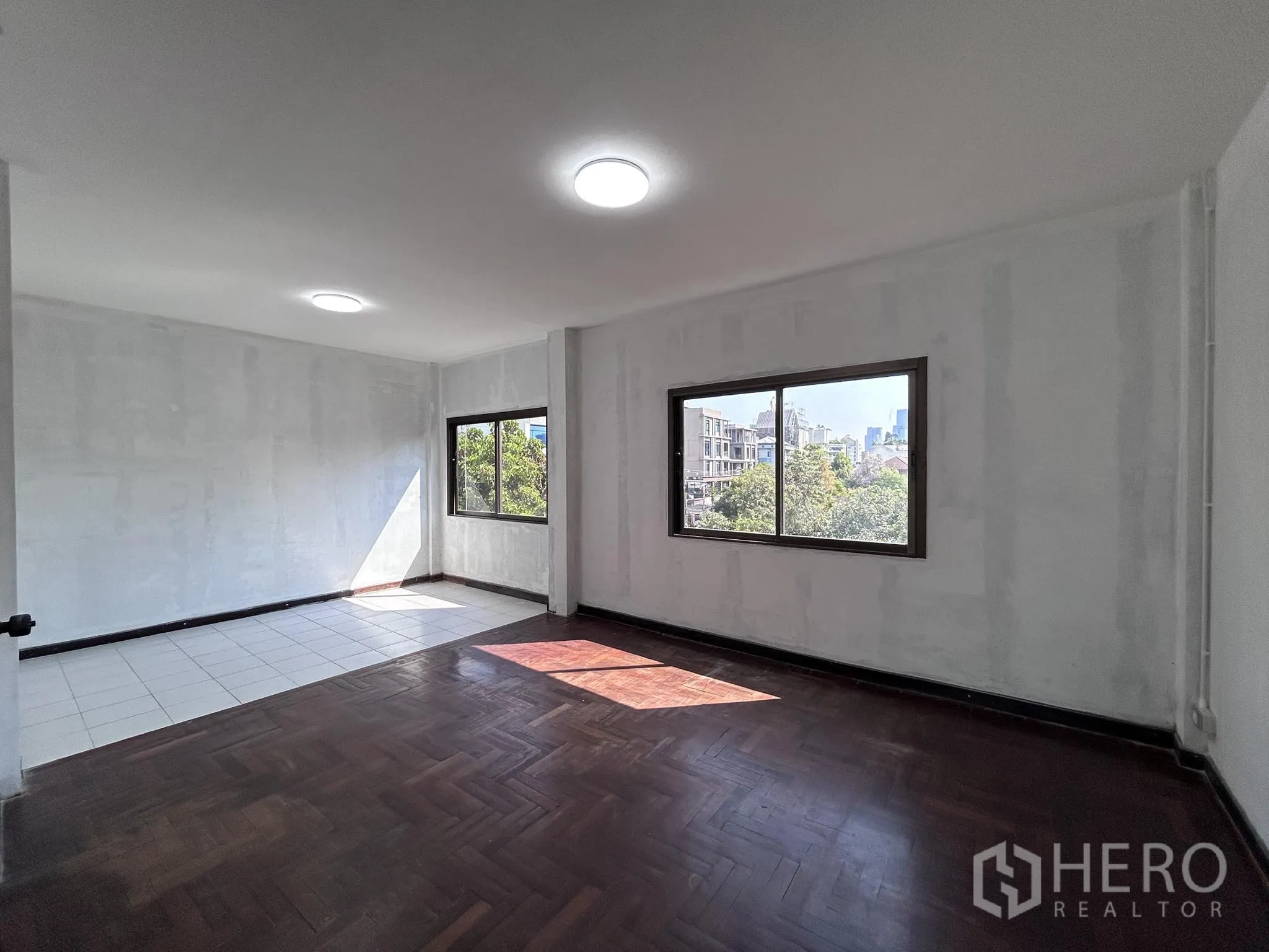 Home Office for rent or sale in Watthana, Bangkok - Corner workspace with mixed tile and wood floors and city-view windows.