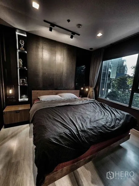 Condominium for sale in Pathum Wan, Bangkok - Bedroom with large window, dark accent wall, and queen bed overlooking greenery.