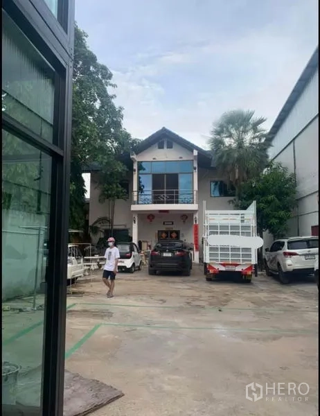 货栈 出租在Sai Noi, Nonthaburi - 院内两层办公楼，前方宽阔停车与车辆