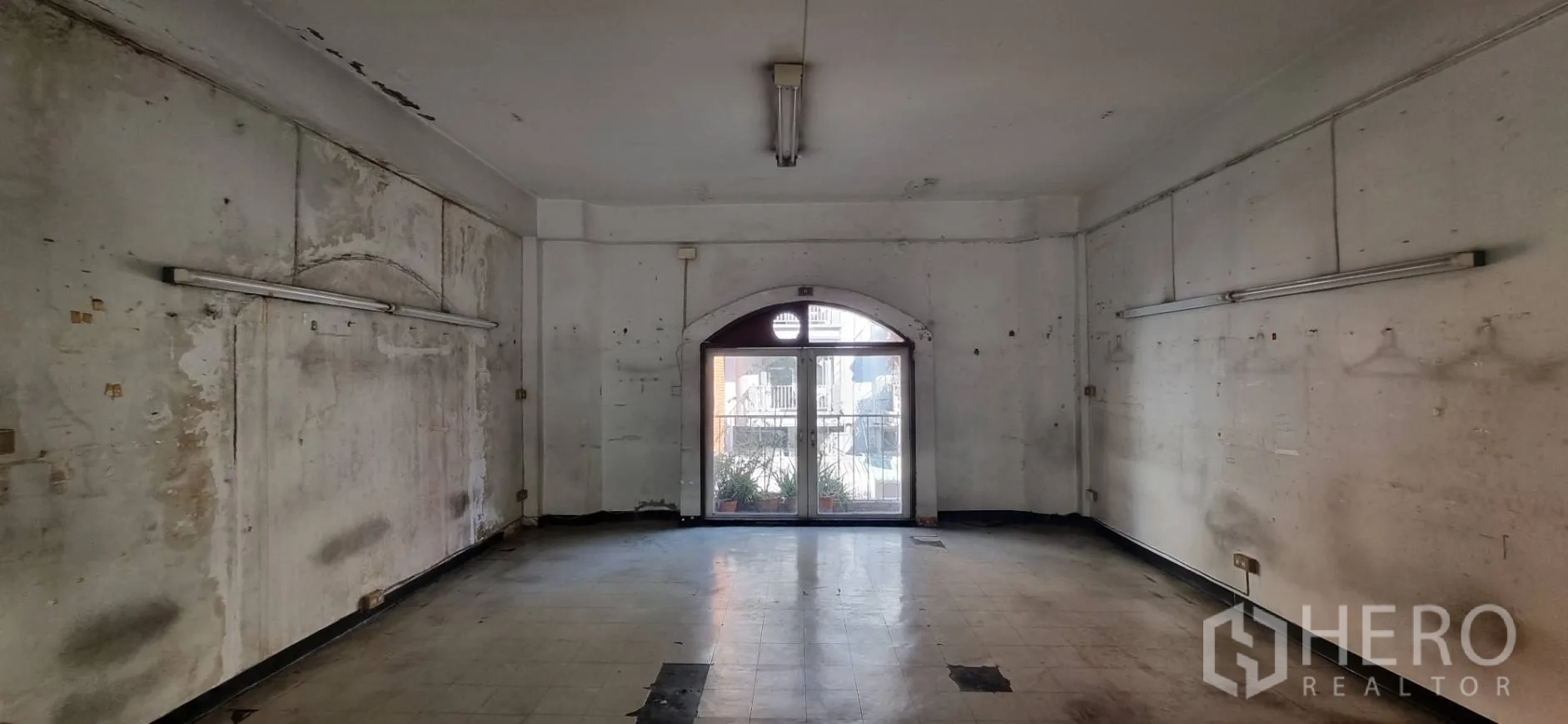Shophouse for rent or sale in Bangkok - Wide room facing balcony planters through arched glass doors, scuffed flooring.
