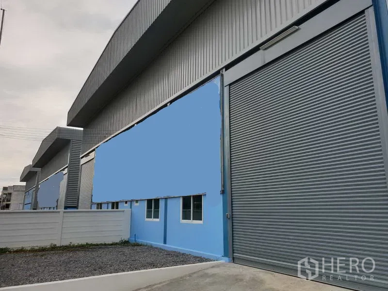 Factory for sale in Sai Noi, Nonthaburi - Modern steel-clad factory exterior with wide roller shutter door and blue facade in Sai Noi, Nonthaburi.