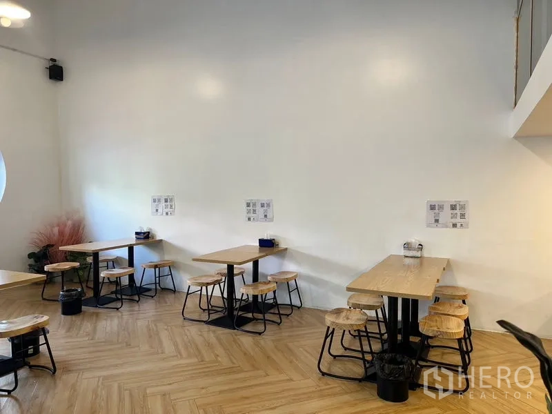 Shophouse for rent in Phra Khanong, Bangkok - Corner seating with minimalist white walls, wooden tables and stools on herringbone flooring.