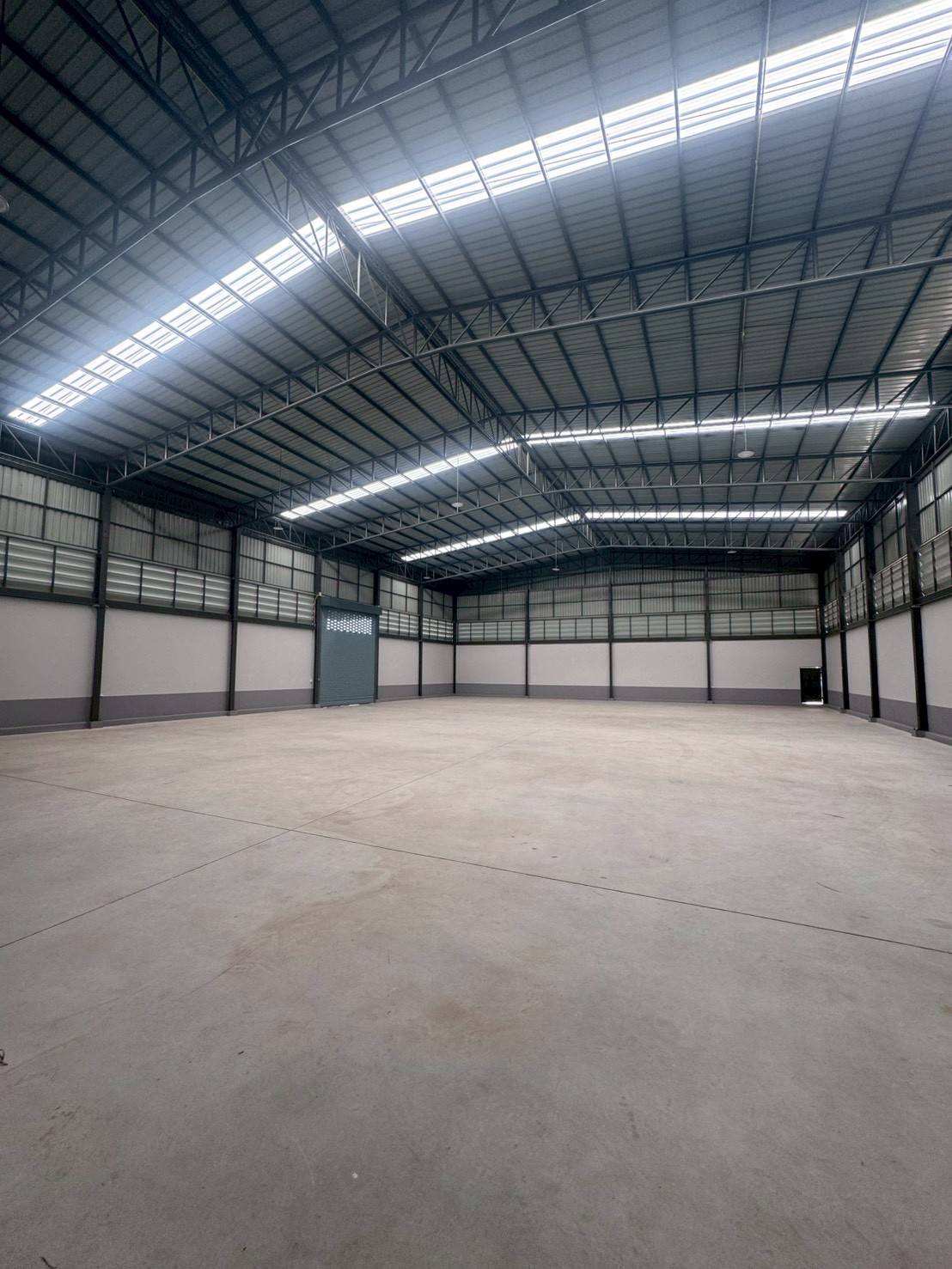 Factory for sale in Mueang Samut Sakhon, Samut Sakhon - Open warehouse floor with curved roof, skylights and wide roller door.