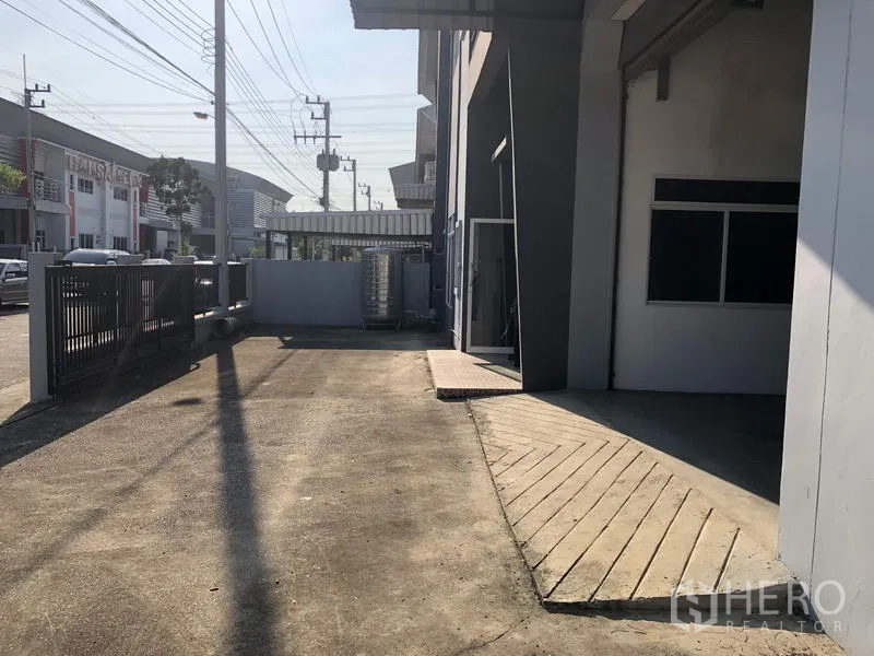 Factory for rent in Lam Luk Ka, Pathum Thani - Side yard access along the building leading to the loading area and sliding gate for trucks.