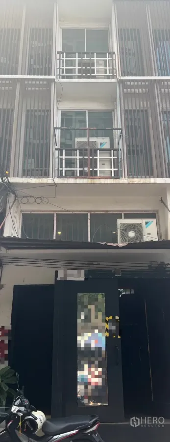 Shophouse for rent in Khlong Toei, Bangkok - Street‑front multi‑storey shophouse with balconies, sliding windows, vertical screens and exterior AC units.