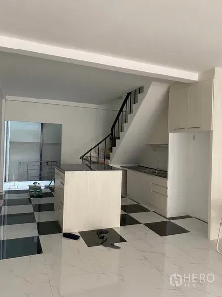 Townhouse for rent or sale in Khlong Toei, Bangkok - Open-plan kitchen and living area with staircase and island on a black-and-white checkered floor