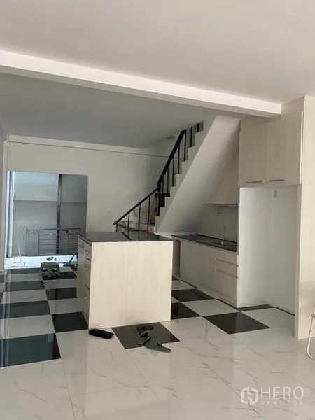 Townhouse for rent or sale in Khlong Toei, Bangkok - Open-plan kitchen and living area with staircase and island on a black-and-white checkered floor