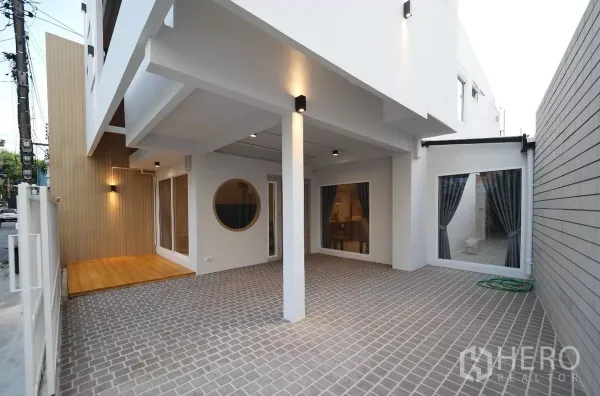 Townhouse for rent or sale in Watthana, Bangkok - Covered carport and tiled courtyard with wood accents and full-height windows.