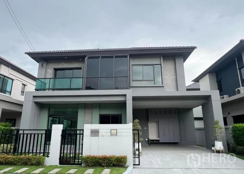 Detached House for sale in Bang Kruai, Nonthaburi - Front elevation of the two-storey house with black metal fence, landscaped lawn and covered parking.