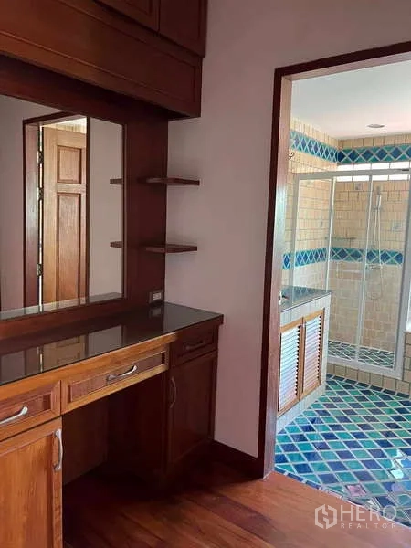 Detached House for rent in Bang Phli, Samut Prakan - Dressing area with wooden vanity leading to a bathroom featuring a glass-enclosed shower and patterned tiles.