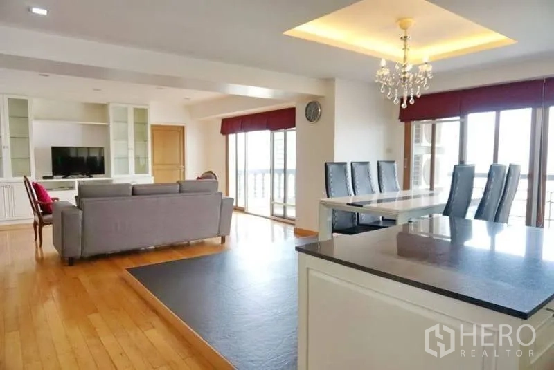 Condominium for rent in Watthana, Bangkok - Spacious living and dining area with chandelier, built-in shelves and large windows opening to a balcony.