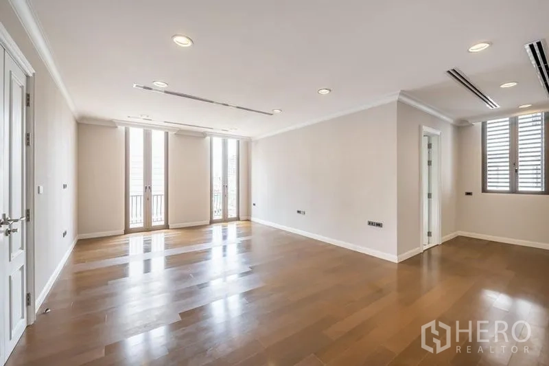 Townhouse for rent in Khlong Toei, Bangkok - Large living area with wood flooring, multiple tall windows and ceiling spotlights.