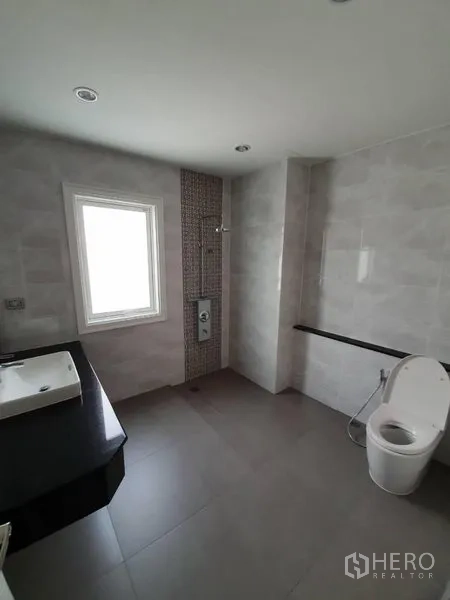 Townhouse for rent in Bang Na, Bangkok - Contemporary bathroom with window, walk-in shower, wall-mounted toilet and black countertop vanity.