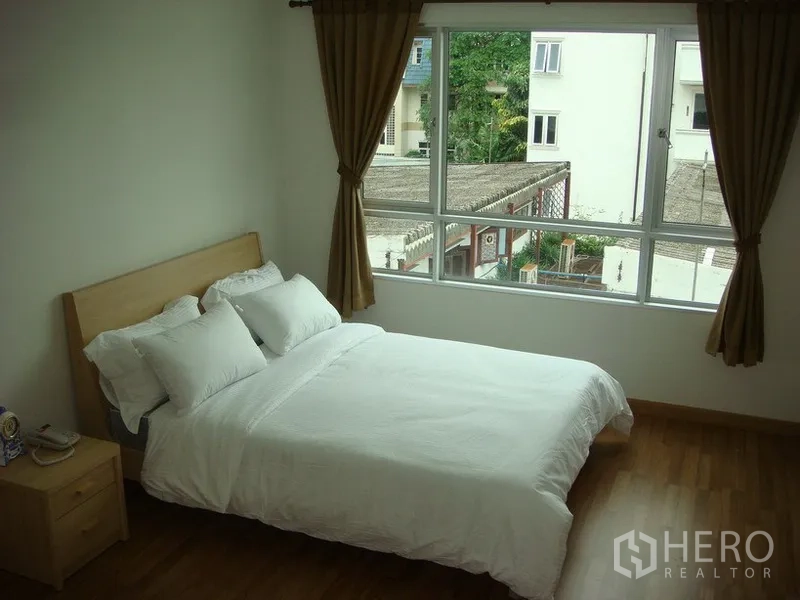 Apartment for rent in Khlong Toei, Bangkok - Bright second bedroom with large window, city and greenery view, curtains, and a double bed.