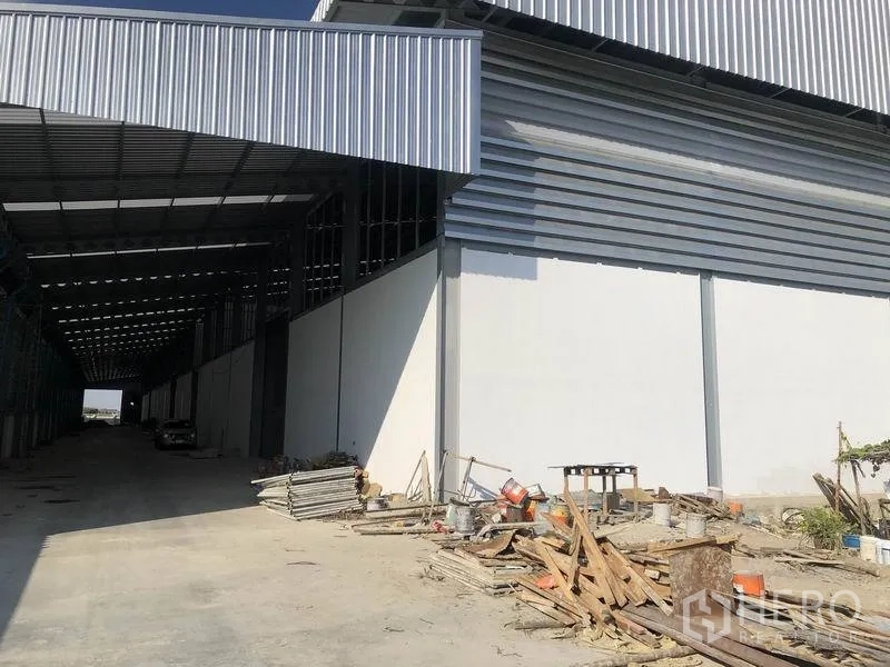 货栈 出租在Bang Phli, Samut Prakan - 仓库侧边带顶装卸区，宽阔车道与堆放的建筑材料。