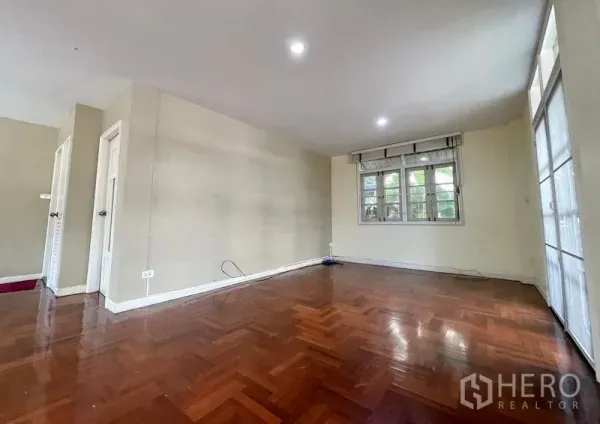 Detached House for rent in Khlong Toei, Bangkok - Spacious living room with parquet wood floors, neutral walls and natural light.