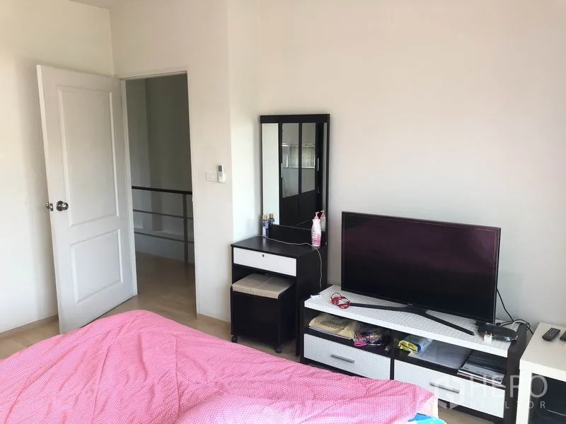 Townhouse for rent or sale in Suan Luang, Bangkok - Cozy bedroom corner with TV console, dressing table and white door.