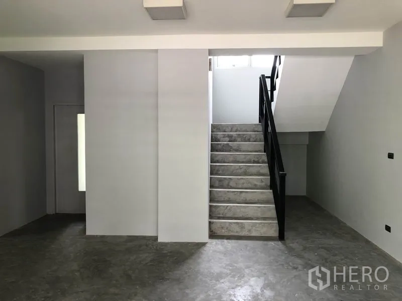 Home Office for rent in Wang Thonglang, Bangkok - Ground-floor interior with polished concrete floors, grey walls, and a staircase with a black handrail.