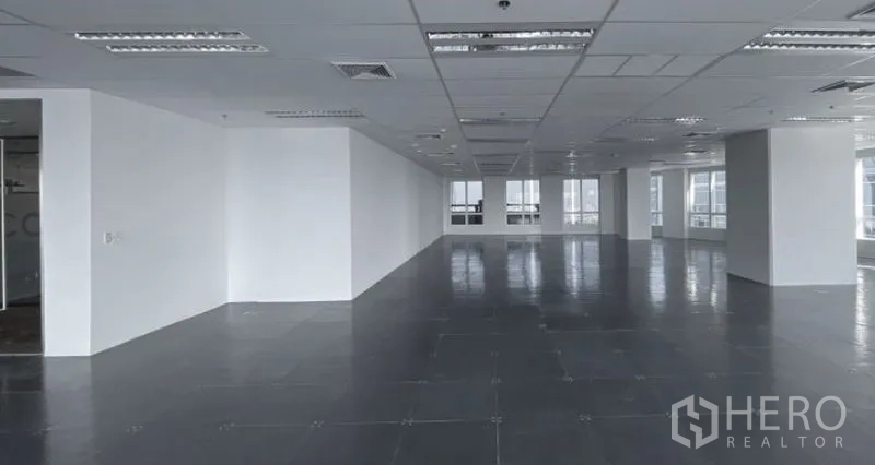 Office Space for rent - Spacious office floor with white columns, suspended ceiling lighting, and rows of windows for natural light.