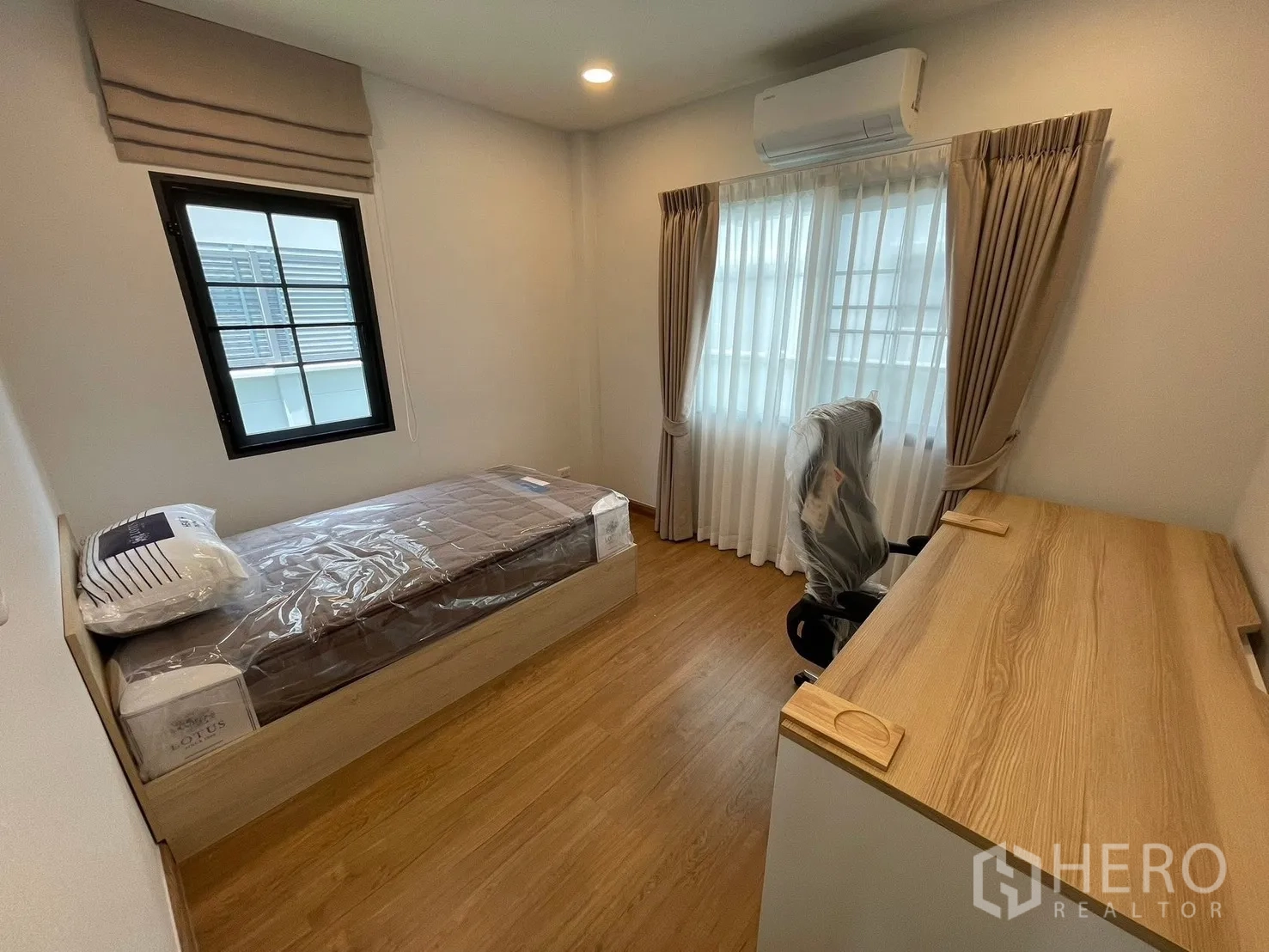 Detached House for rent in Bang Phli, Samut Prakan - Compact bedroom with single bed, wood floors, study desk, and large windows with curtains and wall-mounted air conditioner.