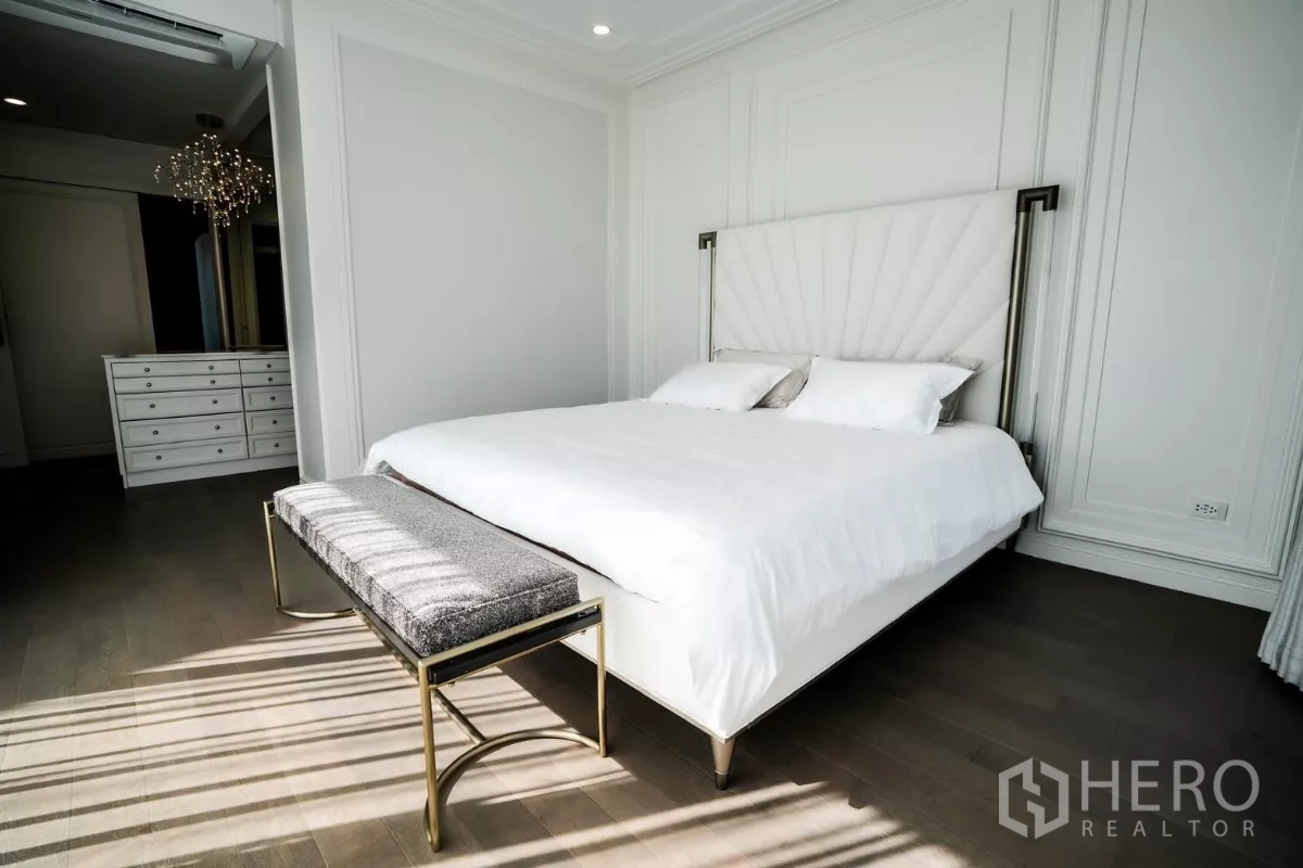 Detached House for rent or sale in Bang Kapi, Bangkok - Sunlit master bedroom with upholstered headboard, bench and hardwood floors.