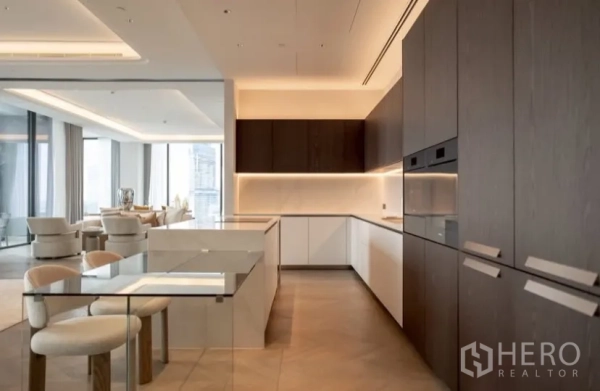 Condominium for rent or sale in Pathum Wan, Bangkok - Sleek kitchen featuring an island breakfast bar, integrated appliances and soft under-cabinet lighting leading to the living room.