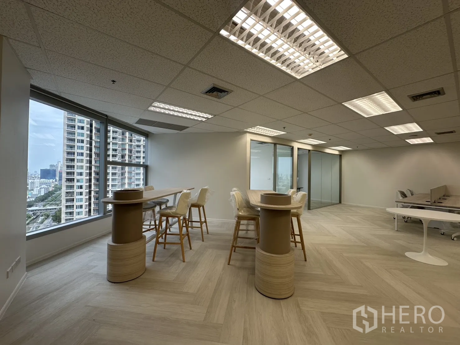 Office Space for rent in Sathon, Bangkok - Bar-height collaboration counter with stools by wide windows next to glass-partitioned rooms.