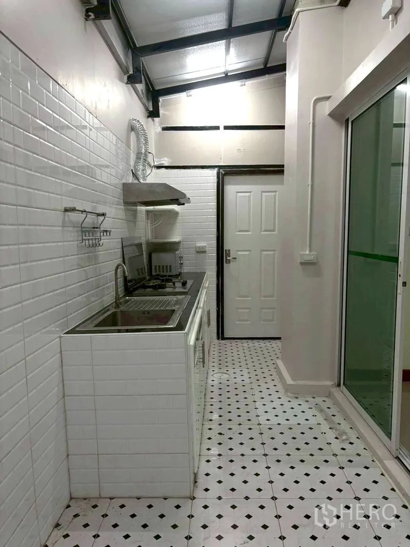 Townhouse for rent in Suan Luang, Bangkok - Enclosed kitchen with gas hob, hood, sink, and white subway tiles.