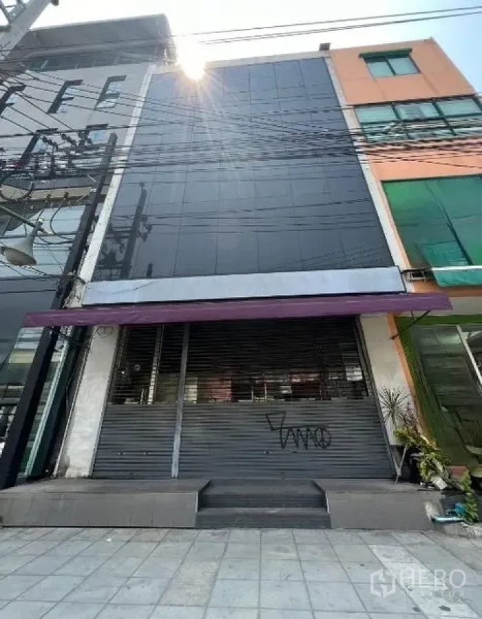 店屋 出租在Watthana, Bangkok - 商铺外立面再视角，黑色玻璃与关闭的卷闸门。