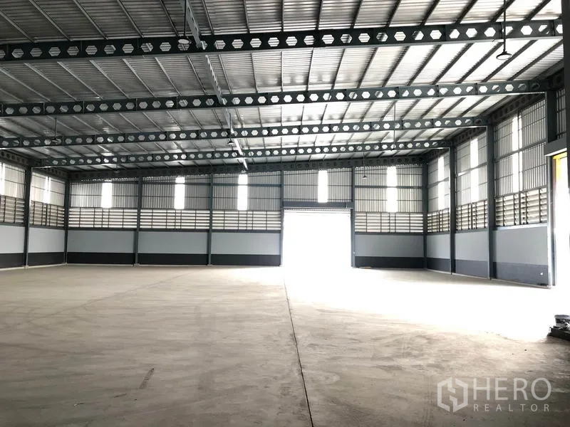 Factory for rent in Bang Len, Nakhon Pathom - Spacious warehouse interior with high steel truss roof and roller shutter door.