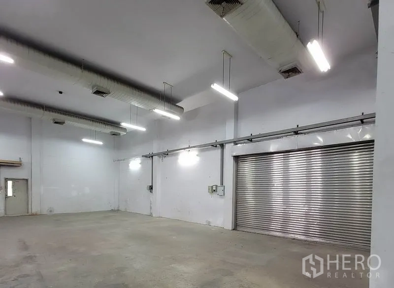 Warehouse for rent in Sam Phran, Nakhon Pathom - Warehouse bay with high ceiling, bright lighting and a large stainless roller shutter.