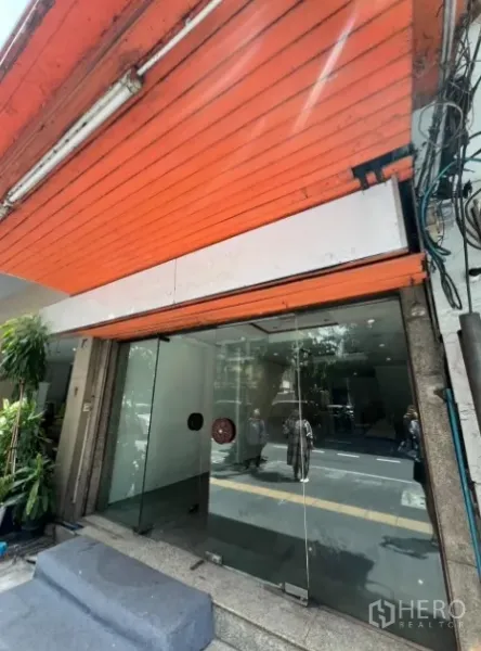 店屋 出租在Khlong Toei, Bangkok - 玻璃双开店门与橙色卷帘门的近景，台阶为花岗岩。