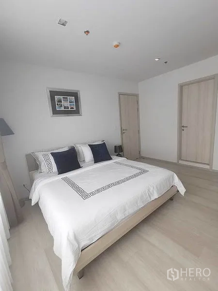 Condominium for rent in Pathum Wan, Bangkok - Spacious bedroom with white bedding and two interior doors.
