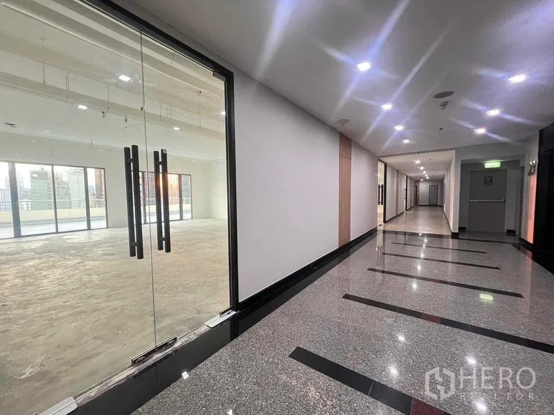 Office Space for rent in Watthana, Bangkok - Modern building corridor with glass double doors leading into a vacant office unit.