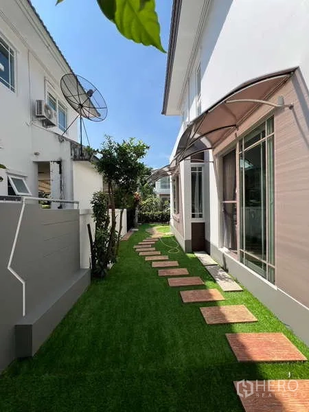 Detached House for rent in Bang Kapi, Bangkok - Side yard walkway with stepping stones and lawn along a modern white façade.