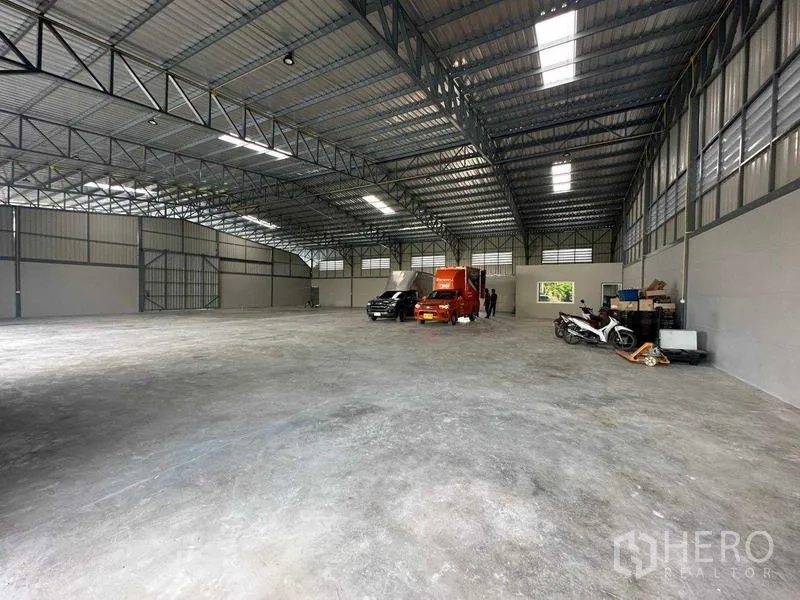Warehouse for rent in Bang Bua Thong, Nonthaburi - Spacious warehouse interior with a high steel truss roof, skylights, and smooth concrete flooring.